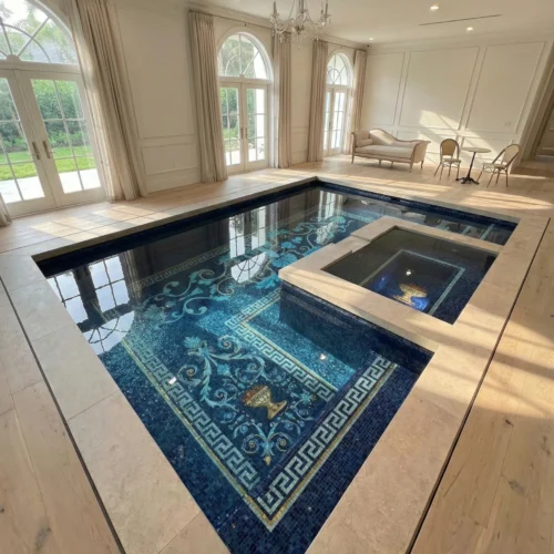 Luxury indoor pool with deep blue mosaic tiles, Greek key border and floral design, featuring a built-in spa, arched windows, and chandelier.