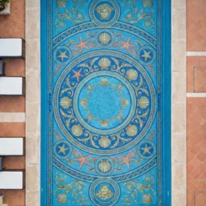 Overhead view of pool with ocean-themed mosaic medallion, seashells and starfish in blue and gold, framed by stone deck and lounge chairs.