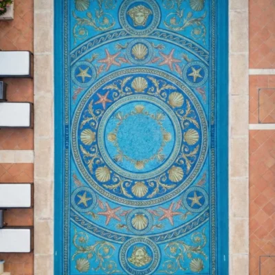 Overhead view of pool with ocean-themed mosaic medallion, seashells and starfish in blue and gold, framed by stone deck and lounge chairs.
