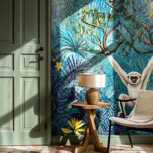 Blue jungle mosaic wall with a white monkey on a tree branch, tropical leaves and flowers beside a chair and table, lit by natural sunlight indoors.