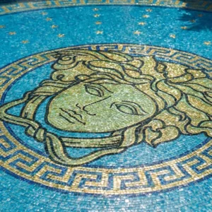 luxury round courtyard pool with Medusa mosaic and Greek key border, surrounded by arches, palm plants and sun loungers.