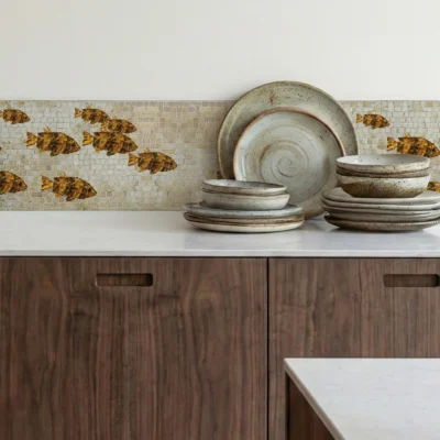 Golden fish mosaic border backsplash above wood cabinets with stacked ceramic plates.