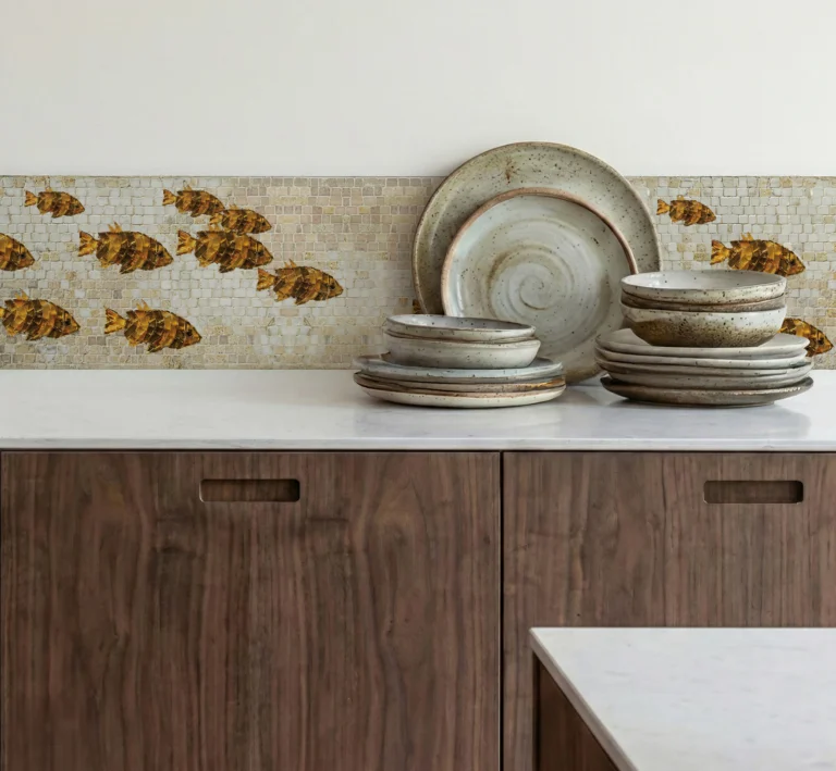 Golden fish mosaic border backsplash above wood cabinets with stacked ceramic plates.