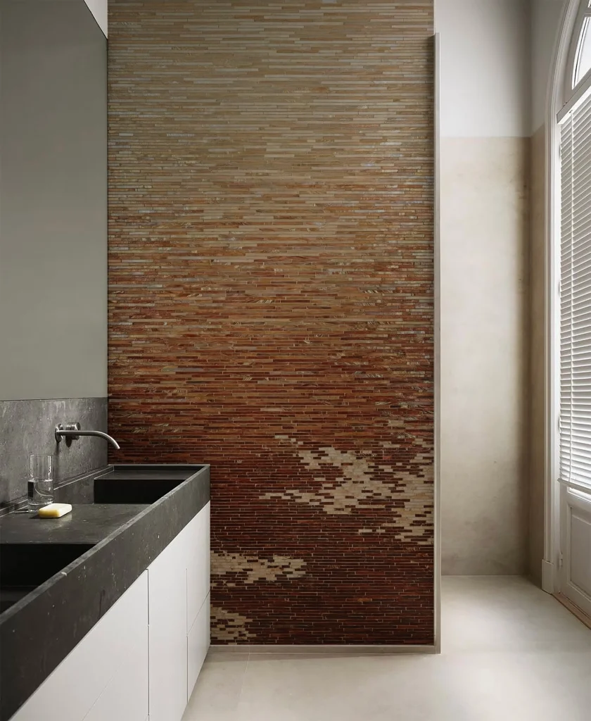Modern bathroom vanity with amber gradient mosaic tile feature wall, dark stone countertop, white cabinets, and soft natural light from window.
