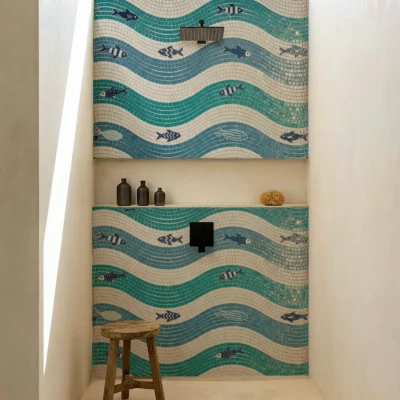 Blue and teal wave mosaic shower wall with fish pattern in a modern coastal bathroom.