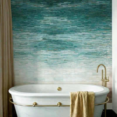Emerald green ombre glass mosaic feature wall behind freestanding bathtub with brass fixtures.