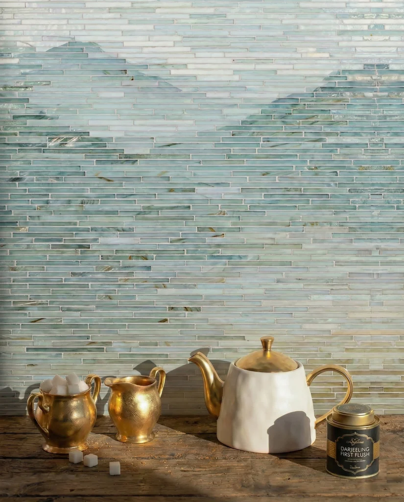 Horizontal seafoam green linear glass mosaic backsplash with brass tea set on wooden counter.