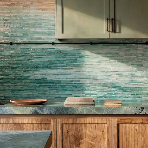 Kitchen backsplash with gradient mosaic tiles in sand to teal tones, paired with wood cabinets and blue stone countertop in warm natural light.