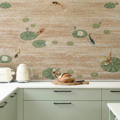 Koi fish and lily pond mosaic backsplash in soft neutral tones above sage green kitchen cabinets.