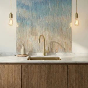 Vertical blue and beige gradient glass mosaic backsplash behind brass faucet in a modern kitchen.
