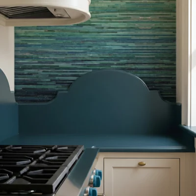 Emerald green and teal linear glass mosaic backsplash with horizontal tiles, adding depth and shine to a luxury kitchen cooktop wall.
