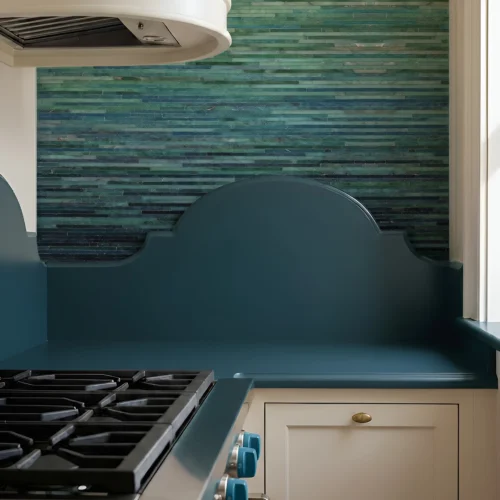 Emerald green and teal linear glass mosaic backsplash with horizontal tiles, adding depth and shine to a luxury kitchen cooktop wall.