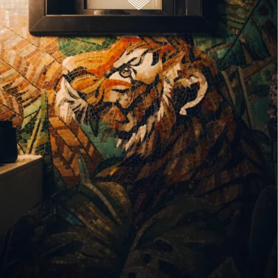 Majestic Tiger mosaic mural with jungle leaves in warm orange and green tones installed on a bathroom wall.