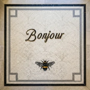 Mosaic tile panel with “Bonjour” script and decorative bee on patterned background.