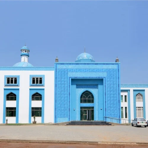 Modern mosque façade with blue geometric mosaic panels, arched entrance and symmetrical architecture reflecting contemporary Islamic design style.