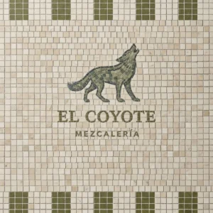 Mosaic signage featuring a green coyote figure with “El Coyote Mezcalería” text on an ivory tile background.