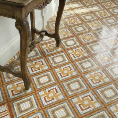 Geometric mosaic floor design with repeating square patterns in warm ochre, terracotta, and grey tones.