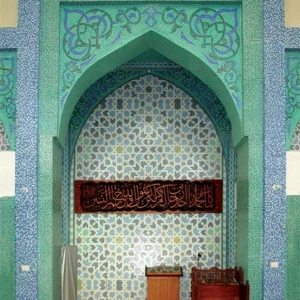 Green Islamic mihrab with geometric star mosaic pattern and Arabic calligraphy panel, showcasing traditional mosque interior design and symmetry.