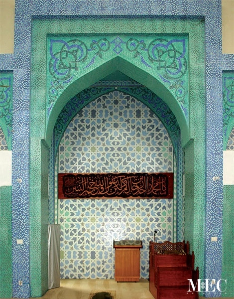 Green Islamic mihrab with geometric star mosaic pattern and Arabic calligraphy panel, showcasing traditional mosque interior design and symmetry.