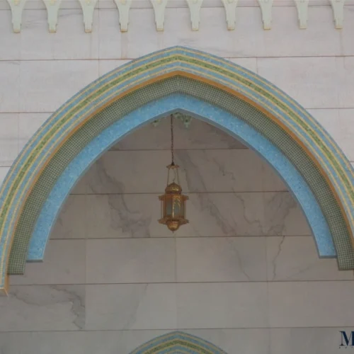 Islamic arch with layered blue, green and gold mosaic borders forming geometric patterns, highlighting traditional mosque architectural detailing.