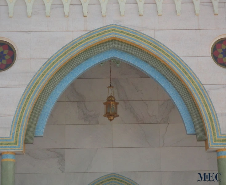 Islamic arch with layered blue, green and gold mosaic borders forming geometric patterns, highlighting traditional mosque architectural detailing.