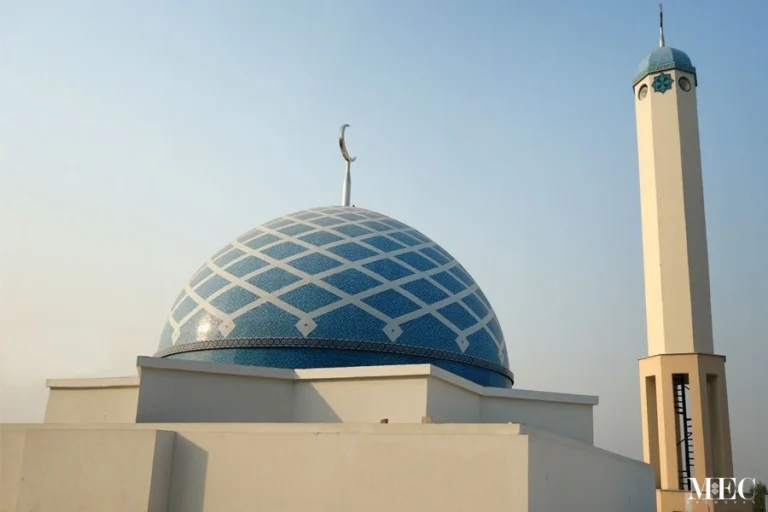 Blue mosque dome with white geometric lattice mosaic pattern and crescent finial, paired with a minimalist minaret in modern Islamic architecture.