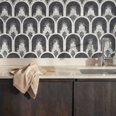 Monochrome mosaic wall with repeating arch patterns in charcoal, grey, and ivory behind a modern kitchen counter.