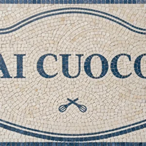 Custom mosaic tile panel with blue name lettering inside decorative cartouche frame.