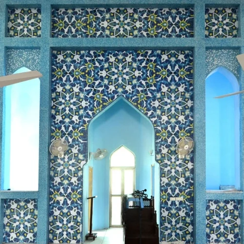 Blue Islamic mosaic wall with floral and geometric patterns surrounding a mosque mihrab, showcasing traditional craftsmanship and symmetrical design.