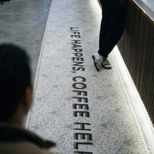 Long mosaic floor runner with “Life Happens Coffee Helps” text in a café setting.
