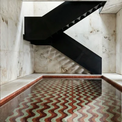 Handcrafted geometric pool mosaic featuring flowing terracotta zigzag patterns with earthy tones beneath reflective water.