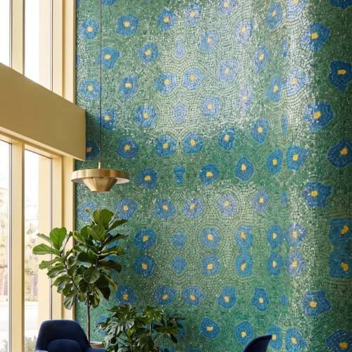 Large handcrafted emerald-green mosaic wall with blue floral motifs creating an artistic botanical statement in a luxury interior.