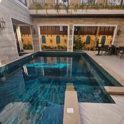 Luxury handcrafted pool mosaic with flowing aqua and deep blue ocean-inspired patterns beneath shimmering reflective water.