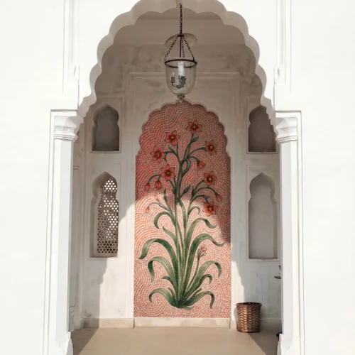 Handcrafted floral mosaic niche featuring blooming flowers and flowing green foliage on a soft pink background within a Mughal-style arch.