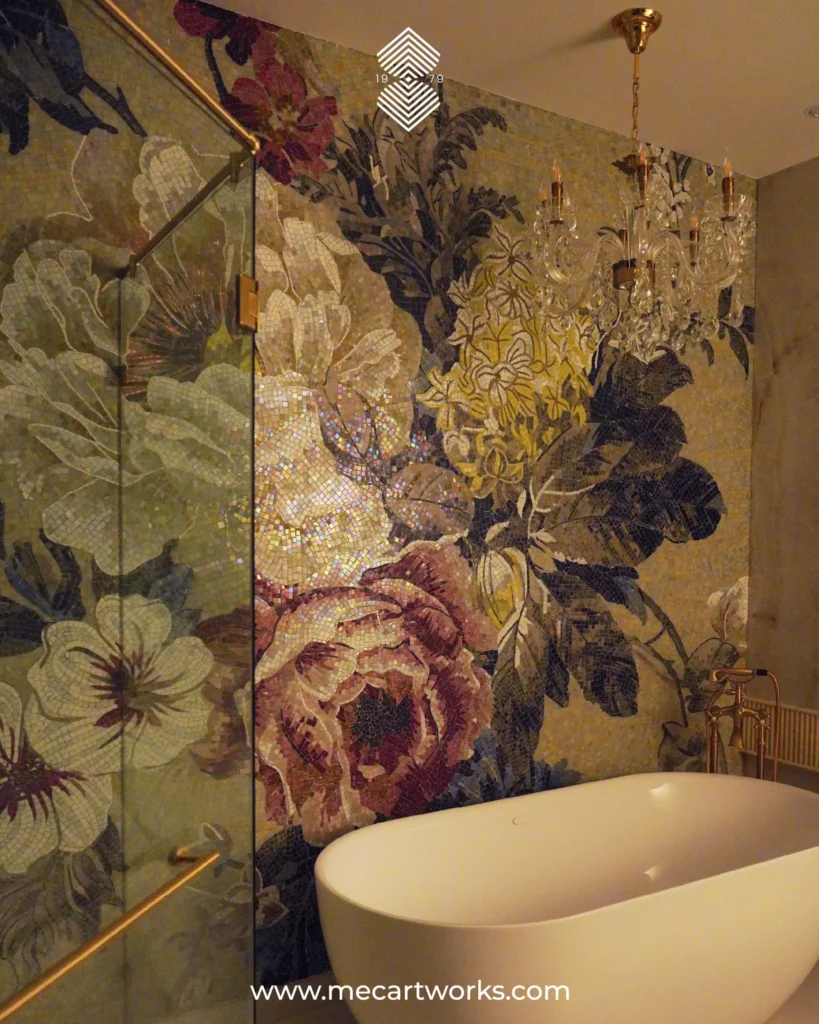A close up of a big classy white bathtub in a slightly dark and dim bathroom, with a stunning custom floral mosaic artwork on the wall behind. It features large, shimmery flowers in subtle tones of pink, green, white, and yellow flowers.