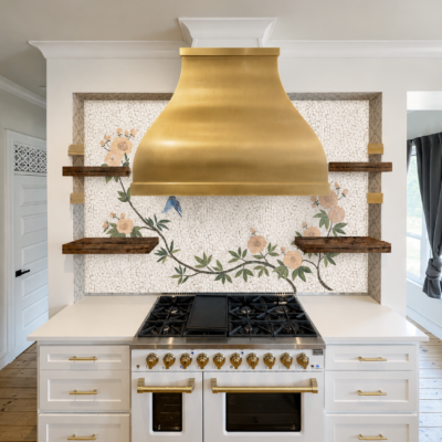 Handcrafted floral mosaic backsplash featuring blooming ivory flowers, green vines, and a bluebird behind a brass kitchen range hood.