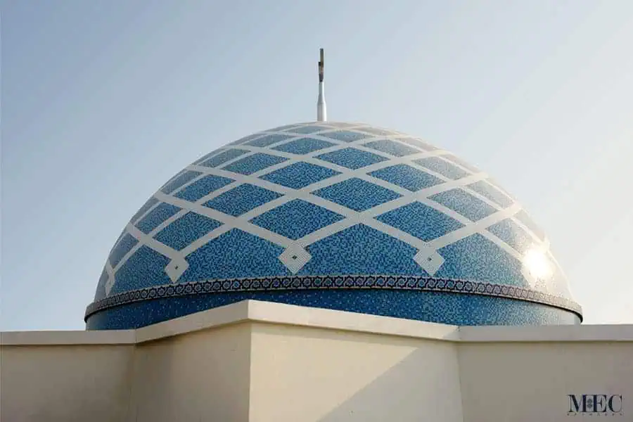 A bright blue architectural dome covered in a mosaic pattern of intersecting white lines and an arabesque border.