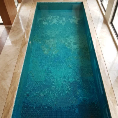 Luxury indoor swimming pool featuring a handcrafted glass mosaic with flowing blue and turquoise aurora-inspired gradients beneath crystal-clear water.