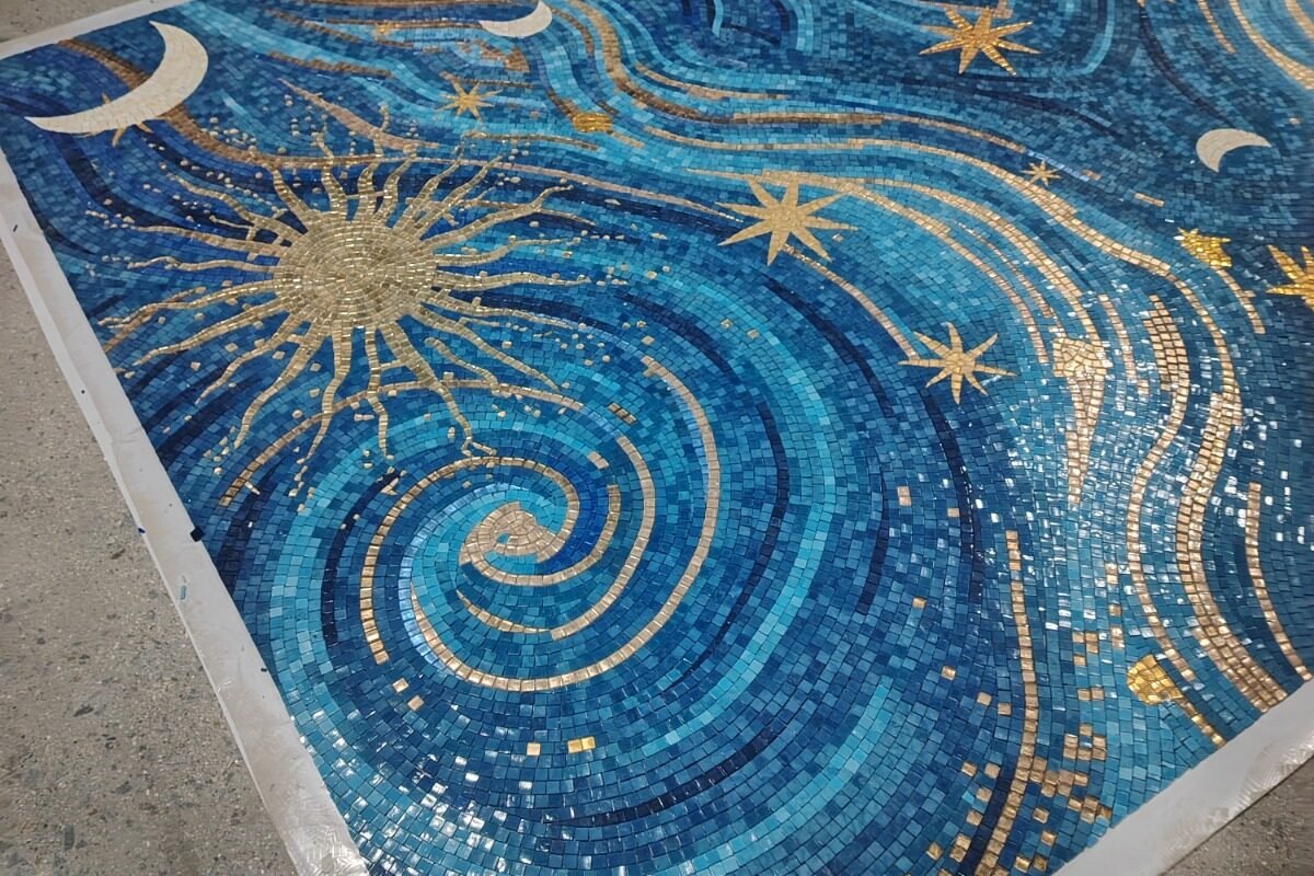 A huge, beautiful mosaic on a workshop floor showing a starry night sky with golden suns and moons.