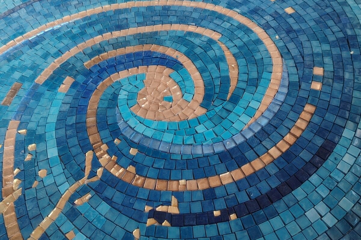 A close-up shot of a tight, mesmerizing spiral pattern made of small dark blue, light blue, and golden glass mosaic tiles.