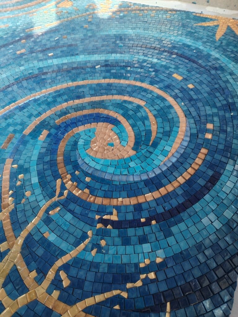 A close-up shot of a tight, mesmerizing spiral pattern made of small dark blue, light blue, and golden glass mosaic tiles.