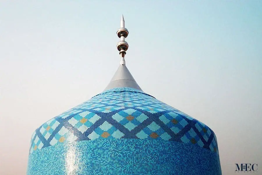 Close-up of a blue mosaic dome featuring a checkered geometric pattern and a metallic finial.