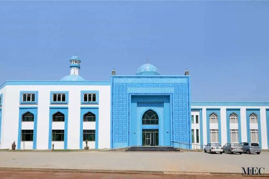 A white building with a prominent arched entrance framed by bright blue mosaic tiles and Arabic calligraphy.