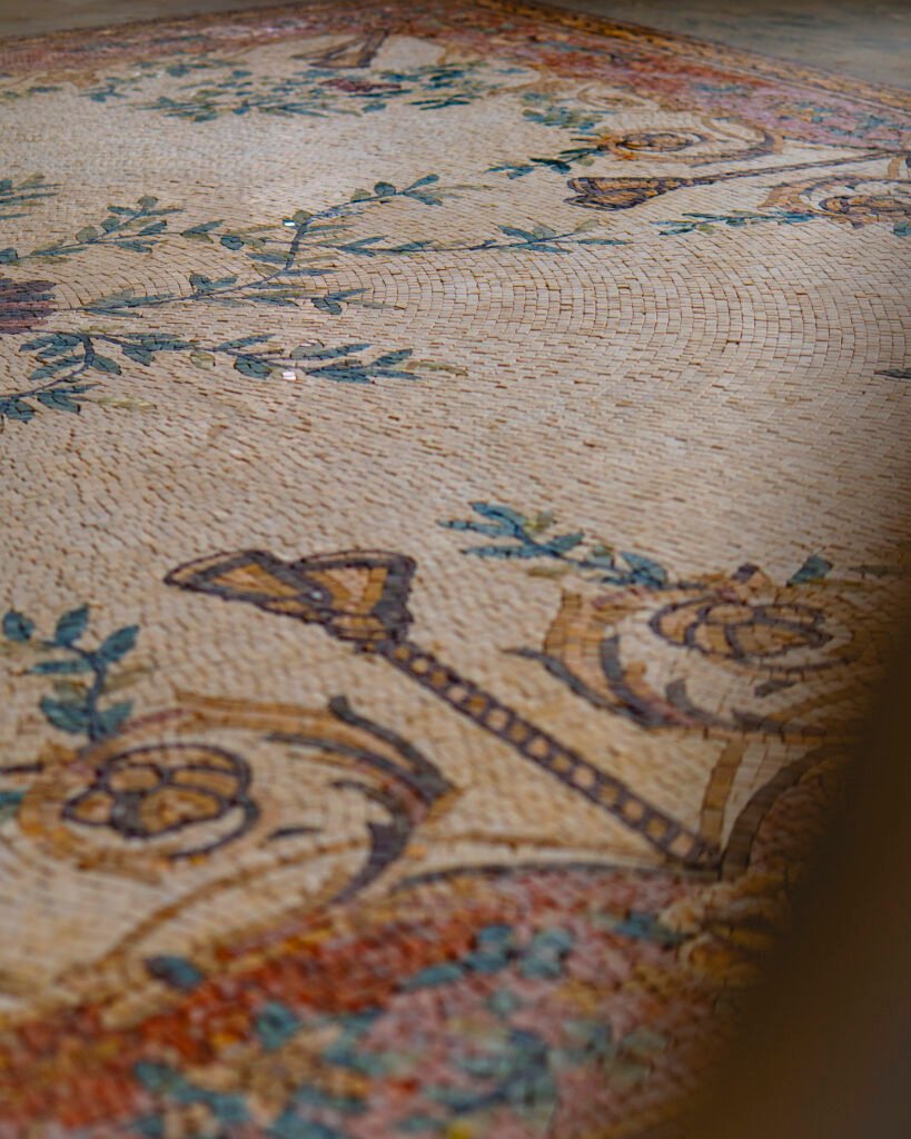 A low-angle perspective of a large, cream-colored mosaic floor designed to resemble a traditional woven rug,