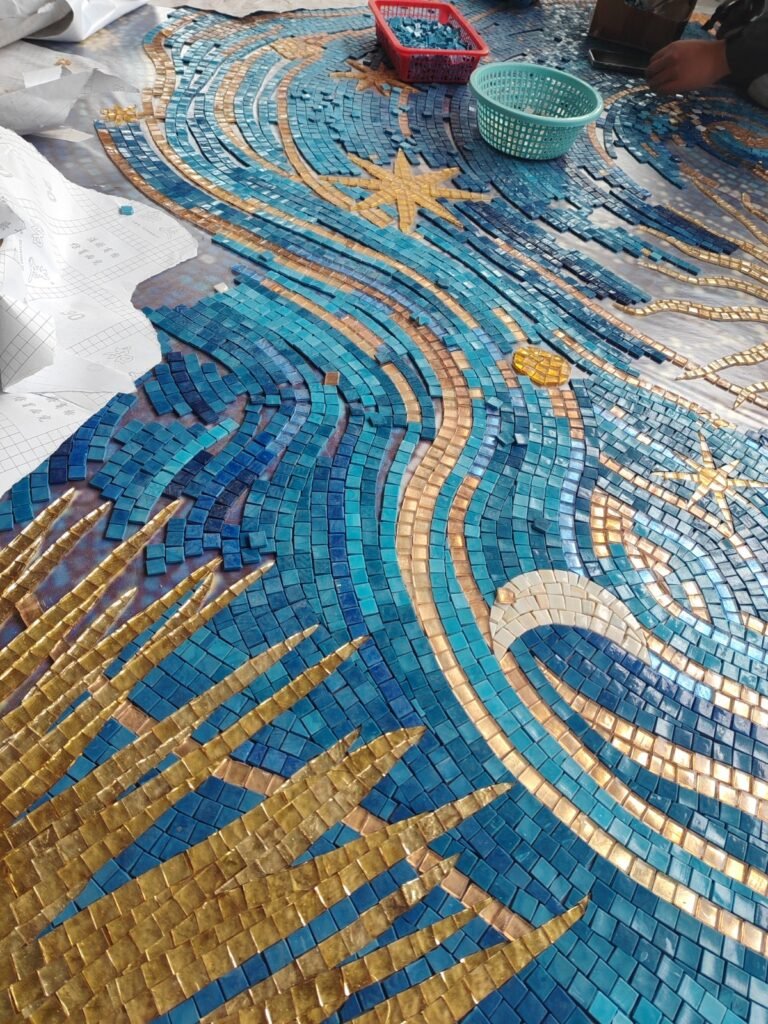 Work in progress of an intricate blue and gold glass mosaic tile pattern being assembled.