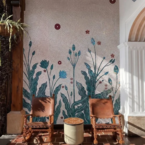 Handcrafted botanical mosaic mural with teal leaves, tall flowers, burgundy blossoms, and flowing ivory background tesserae.
