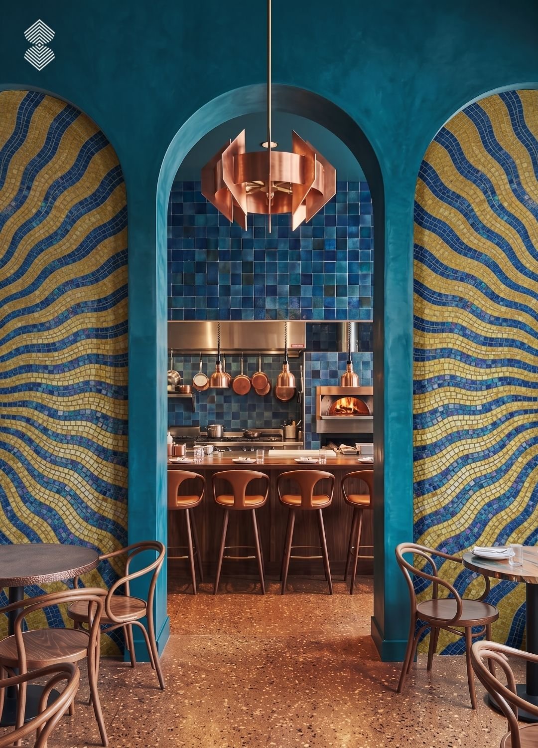 High-arch doorway framing a view into an open kitchen with copper pans and a pizza oven, flanked by vibrant blue and yellow wavy mosaic walls.