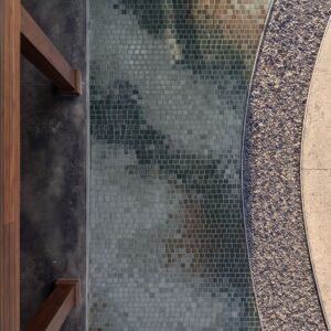 A close overhead view of an abstract stone walkway mosaic in green, taupe, and rust tesserae running alongside a curved gravel path.