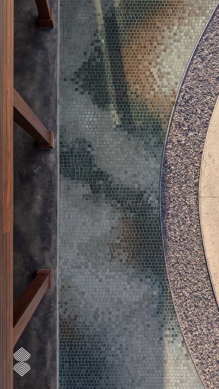 A close overhead view of an abstract stone walkway mosaic in green, taupe, and rust tesserae running alongside a curved gravel path.