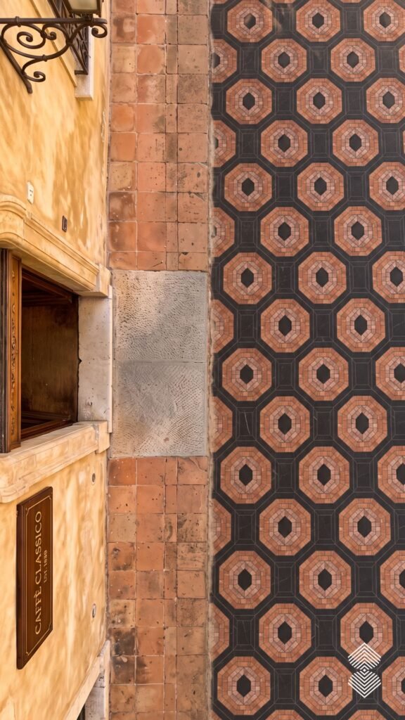 Top-down perspective of a mosaic walkway featuring flowing wave patterns in shades of cream, tan, and dark brown stone.